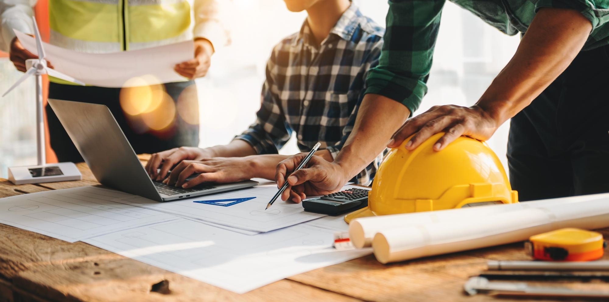tres-colegas-discutindo-o-trabalho-de-dados-e-o-laptop-tablet-com-um-projeto-arquitetonico-no-canteiro-de-obras-na-mesa-do-officexa